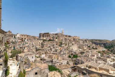 Matera - Basilikata - Italien - 06-16-2025: Güneşli bir günde açık mavi bir gökyüzünün altında Matera, İtalya 'nın yamaçlarındaki tarihi taş binaların panoramik bir görüntüsü.