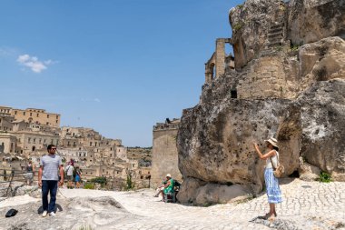 Matera - Basilikata - Italien - 06-16-2025: Tourists walking and taking photos near historic cliffside buildings in Matera, Basilicata, under a clear blue summer sky.
