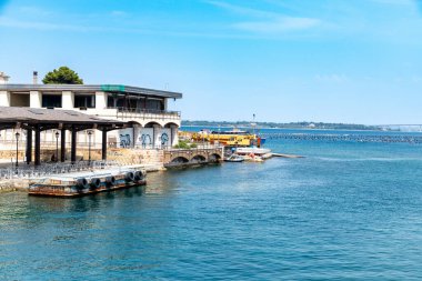 Taranto - Puglia - Italien - 06-17-2025: Rıhtımlı tekneleri, kemerli destekleri, terası ve açık güneşli bir günde mavi denizi olan grafiti kaplı bina.