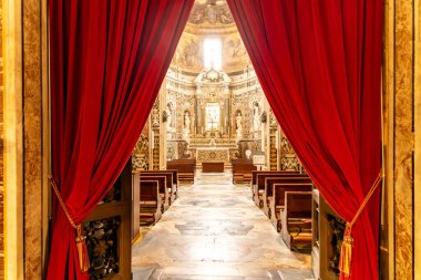 Taranto - Puglia - Italien - 06-17-2025: View through red curtains into a richly decorated chapel with benches, marble altar, gold ornaments and detailed ceiling frescoes.