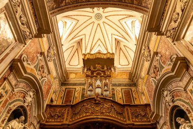 Taranto - Puglia - Italien - 06-17-2025: Oyma ahşap bir balkonun üzerinde altın detaylarıyla barok boru orgu, kırmızı çizgili ve tavan pencereli beyaz bir tavanın altında yer alıyor..