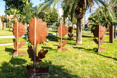 Reggio Calabria 'da, palmiye ağaçları ve modern kentsel binalarla çevrili çimenli bir çimenlikte çeşitli şekillendirilmiş kahverengi çiçek heykelleri duruyor..