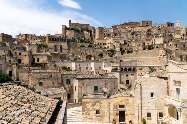 Matera, Basilicata 'daki tarihi taş binaların ve teraslı çatıların panoramik manzarası. Parlak bir yaz gününde, parçalı bulutlu gökyüzünün altında..