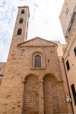 Taranto, İtalya 'da kemerli camları ve çan kulesi olan tarihi kilise cephesi, bitişik binalar arasında dar bir sokaktan görülüyor..