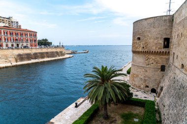Taranto - Puglia - Italien - 06-17-2025: Kızıl bir bina, kale duvarı, palmiye ağacı, rıhtım gezisi ve deniz manzarası.