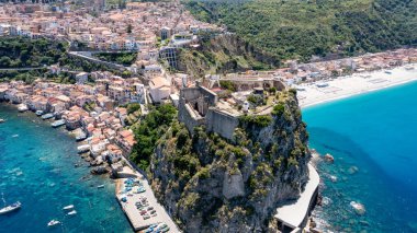 Scilla 'lı Castello Ruffo turkuaz denizin üzerindeki dik bir uçurumda, Güney Calabria' da tarihi binalar ve plajlar berrak gökyüzünün altında..