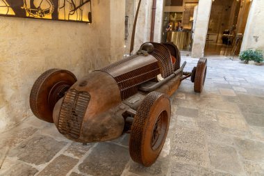 Lecce - İtalya - 06-21-2025: Ayrıntılı lastik desenleri ve İtalya 'nın Lecce kentindeki görünür bileşenleriyle kapalı alanda sergilenen klasik bir yarış arabasının tam ölçekli ahşap heykeli.