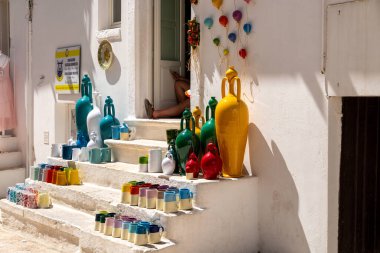 Locorotondo - Apulien - İtalya - 06-25-2025: Locorotondo 'da beyaz merdivenlerde renkli seramik sürahiler ve kupalar.