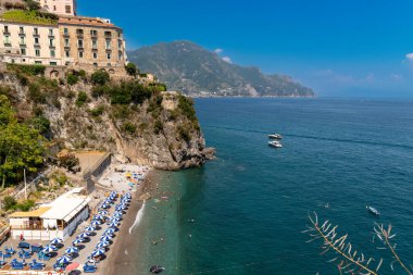Amalfikueste - Kampanien - Italien - 07-04-2025: Güneşli bir yaz gününde Amalfi Kueste boyunca binalarla kaplı şemsiyeli, banyolu ve kayalık bir uçurum manzarası.