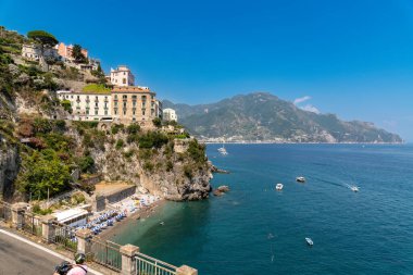 Amalfikueste - Kampanien - Italien - 07-04-2025: Güney İtalya 'da bir sahil kayalıklarında şemsiyeli, güneşli, yüzücü ve tekneli binalar. Amalfi Kueste