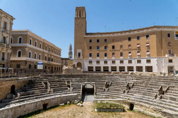 Lecce - Lecce - İtalya - 06-21-2025: Lecce 'deki Roma amfitiyatrosu modern binalarla çevrili ve INAIL binası arena merdivenlerinin arkasında belirgin bir şekilde görülüyor.
