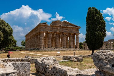 Capaccio Paestum - Kampanien - Italien - 07-06-2025: Paestum 'da Doric sütunları olan antik bir Yunan tapınağının manzarası, kısmen ağaçlar, taş kalıntıları ve parlak bir yaz gökyüzü ile çevrili.