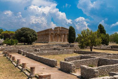 Capaccio Paestum - Kampanien - Italien - 07-06-2025: Taş kalıntıları ve ağaçlarla çevrili Antik Yunan tapınağı, arka planda dramatik bulutlar ve Paestum 'daki Doric sütunlarının berrak manzarası.