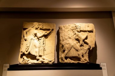 Capaccio Paestum - Kampanien - Italien - 07-06-2025: Kapalı alanlarda sergilenen iki antik taş kabartması, yüksek rahatlama ve yapay ışık tarafından aydınlatılan insan figürlerini gösteriyor.