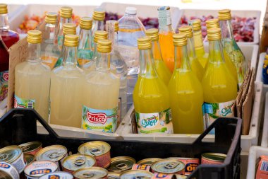 Capaccio Paestum - Kampanien- Italien- 07-10-2025: Etiketli sarı ve soluk renkli içecek şişeleri, gündüz saatlerinde bir markette çeşitli konserve ürünleriyle birlikte sandıklarda sergileniyor.