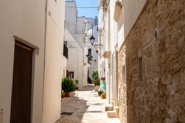 Locorotondo 'da duvarları beyazlatılmış, saksı bitkileri, taş kaldırım ve duvara asılmış klasik bir sokak feneri olan dar bir sokak..