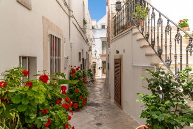 Locorotondo 'da dar bir sokakta çiçek saksıları ve demir merdivenler, beyaz duvarlar ve parlak bir yaz gökyüzünün altında taş kaldırımlar..