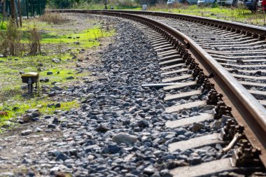 Madalyon - Karlovy Vary - Çek Cumhuriyeti - 09-24-2022: Arka planda yeşil çimenler ve park halindeki çok sayıda araçla güneşli bir alanda çakıl ağırlıklı kavisli tren yolu.