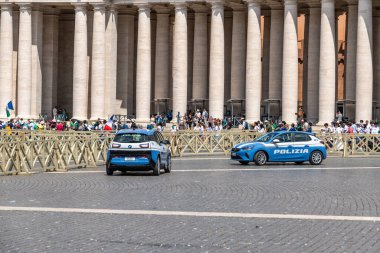 Roma - Lazio - İtalya - 08-02-2025: St. Peters Meydanı 'ndaki taş sütunların önünde iki polis aracı park ederken, turistler arka plandaki bariyerler boyunca yürüyorlar.