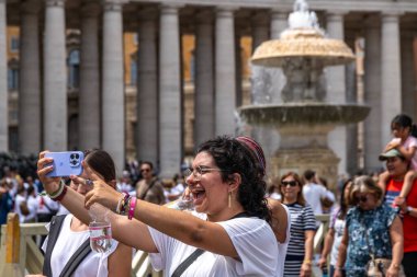 Roma - Lazio - İtalya - 08-02-2025: İki gülümseyen kadın Vatikan 'daki St. Peters Meydanı' ndaki kalabalık arasında büyük bir çeşme ve uzun sütunlar önünde selfie çekiyor.