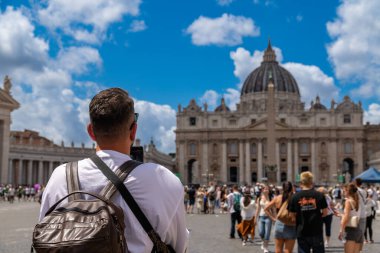 Roma - Lazio - İtalya - 08-02-2025: Sırt çantalı bir adam St. Peters Bazilikası 'nın ve St. Peters Meydanı' ndaki dikilitaşın önünde fotoğraf çekiyor.