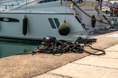 Nydri - İyon Adaları - Yunanistan - 08-07-2025: Durgun su yüzeyinin yanında asılı çamurluklarla kenetlenmiş yatın yanında, iskelede zincirli ve sarmalanmış halatla demirlenmiş siyah halat.