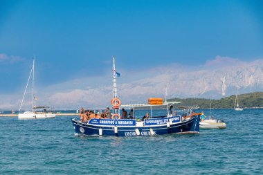 Nydri - İyon Adaları - Yunanistan - 08-07-2025: Lefkas yakınlarındaki mavi denizi aşan ve arka planda dağları ve diğer gemileri görebilen insanlarla dolu bir yolcu gemisi.