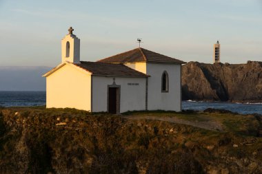 Virxe do Porto (Valdovino) hermitage and Punta Frouxeira lighthouse with the cliffs in the Rias Altas touristic area of Galicia at sunset, Meiras, Spain. clipart