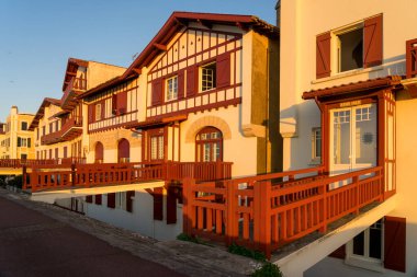 SAINT JEAN DE LUZ, FRANCE - SEPTEMBER 04, 2022: Jacques Thibaud 'daki geleneksel Bask evleri, Frech' in güzel Bask kasabası Saint Jean de Luz köyünde gün batımında büyük plajın önünde yürürler..