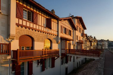 SAINT JEAN DE LUZ, FRANCE - SEPTEMBER 04, 2022: Jacques Thibaud 'daki geleneksel Bask evleri, Frech' in güzel Bask kasabası Saint Jean de Luz köyünde gün batımında büyük plajın önünde yürürler..