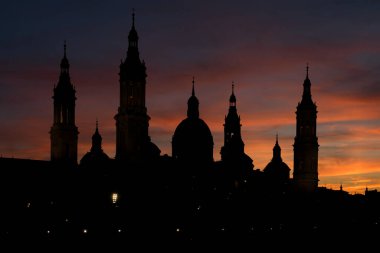 Zaragoza şehrinin Pilar Bazilikası, gün batımında dramatik bir gökyüzü ile Ebro Nehri 'ni yansıttı. Aragon, İspanya.