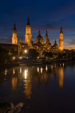 Zaragoza şehrinin Pilar Bazilikası, gün batımında dramatik bir gökyüzü ile Ebro Nehri 'ni yansıttı. Aragon, İspanya.