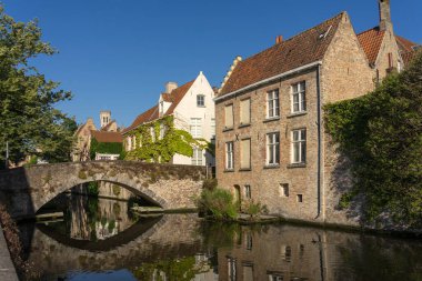 BRUGGE, BELGIUM - 06 Temmuz 2023: Peerden Köprüsü ve tarihi binalar güneşli bir günde Belçika 'nın güzel Brugge kentinin eski kasabasındaki kanala yansıdı.