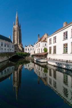 BRUGGE, BELGIUM - 07 Temmuz 2023: Güneşli bir günde Belçika 'nın güzel Brugge kentinin eski kanalı Dijver Parkı ile Lady Kilisesi kulesinin kesiştiği günden beri kanalda iskele.