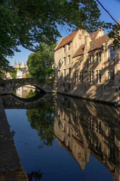 stock image BRUGGGE, BELGIUM - JULY 06, 2023: Meestrat bridge and historic buildings reflected on the canal in the old town of the beautiful city of Brugge in Belgium in a sunny day.