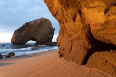 Santa Cruz plajı ünlü doğal kemer düzeniyle gün batımında, Portekiz.