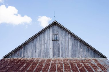Paslı metal çatılı eski bir ahır ve üzerinde rüzgar gülü olan yıpranmış bir kaplama.. 