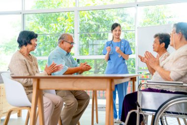 Asyalı doktor ya da hemşire, üst düzey kadın ve erkek gruplarını mutluluk için cesaretlendirir ve yaşlılar sağlık kliniğinde iyi duyguları ifade etmek için el çırparlar..