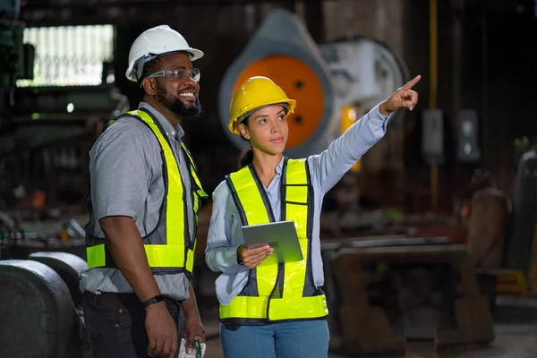 African American factory worker smile and stand with his coworker point and explain about work in industrial workplace area. Concept of happiness with teamwork together and support business.