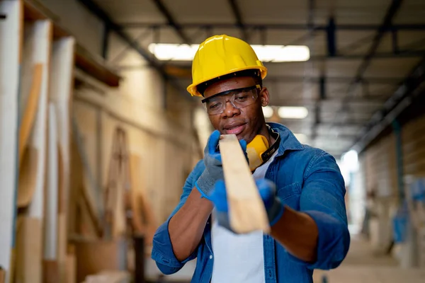 African American carpenter man hold timber or wood stick also look forward to check quality of wood product in factory workplace.