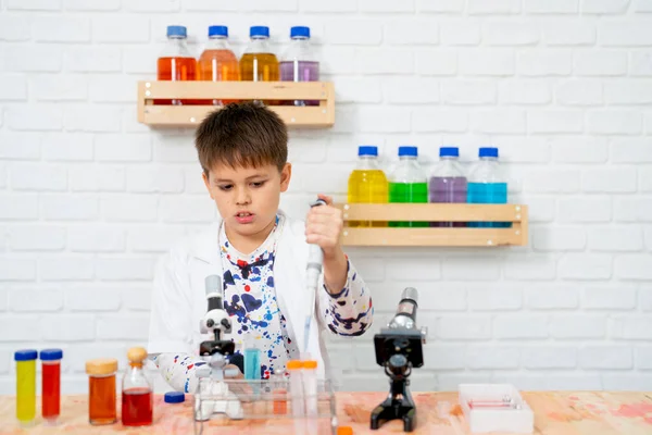 在学校的科学课上 小男孩穿上实验服 作为初级科学家 并运用自动吸管进行实践 — 图库照片