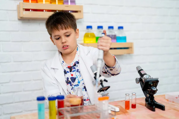在学校的科学课上 小男孩穿上实验服 作为初级科学家 并运用自动吸管进行实践 — 图库照片