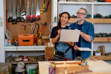 Kafkasyalı marangoz, elinde odunla çalışan Asyalı eşiyle birlikte fabrikada çalışıyor ve projelerinden memnun görünüyorlar..