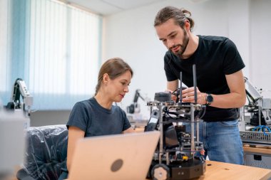 Kafkasyalı profesyonel mühendis ya da teknisyen, fabrika işyerindeki masaya yerleştirilen küçük robotik makineyi kontrol ve bakım için günlük kıyafet işçileri.