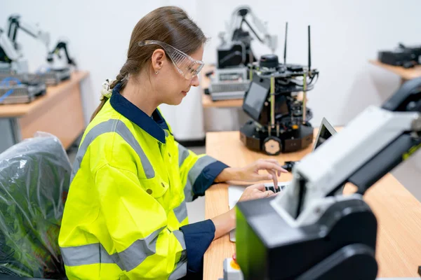 Caucasian technician or engineer worker use laptop to maintenance and check the system of small robotic machine on table in factory workplace.