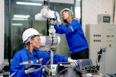 İki profesyonel mühendis veya teknisyen kadın kalite kontrol sistemine sahip fabrika işyerindeki robotik kol makinesinin kontrol ve bakımına yardım ediyor..