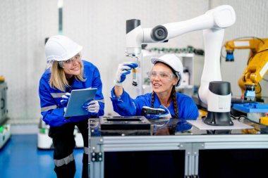 İki profesyonel teknisyen veya mühendis kadının ön görüntüsü oturur ve fabrika işyerindeki robotik makine ile sistem kontrol ve ipad yardımcı olur.