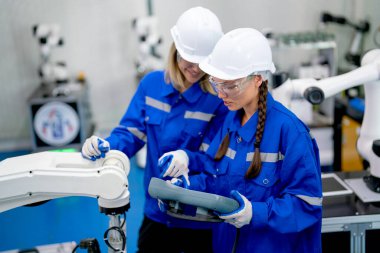 İki profesyonel mühendis ya da teknisyen kadın fabrika robotlu kol makinesinin kontrolörüyle tartışıyor ve onunla çalışıyor..