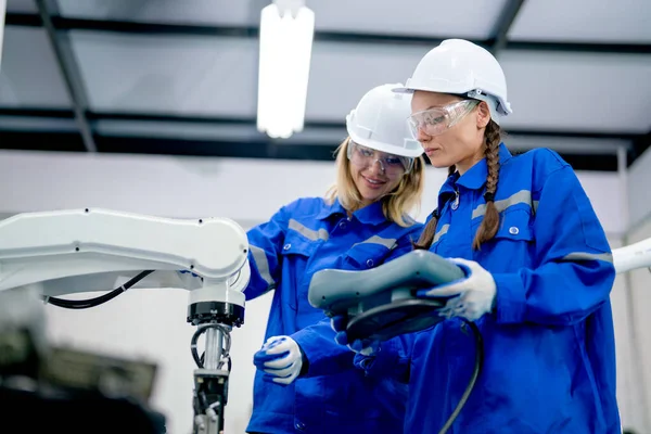 Lower view of two professional engineer or technician worker women discuss and work using controller of factory robotic arm machine.