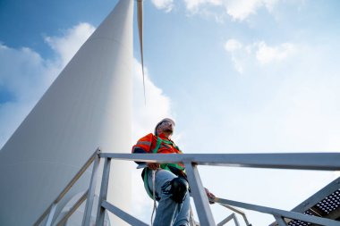 Kafkas mühendisi ya da teknisyen yel değirmeni ya da rüzgar türbininin tabanında yürür ve mavi gökyüzüne ve gün ışığına bakar..
